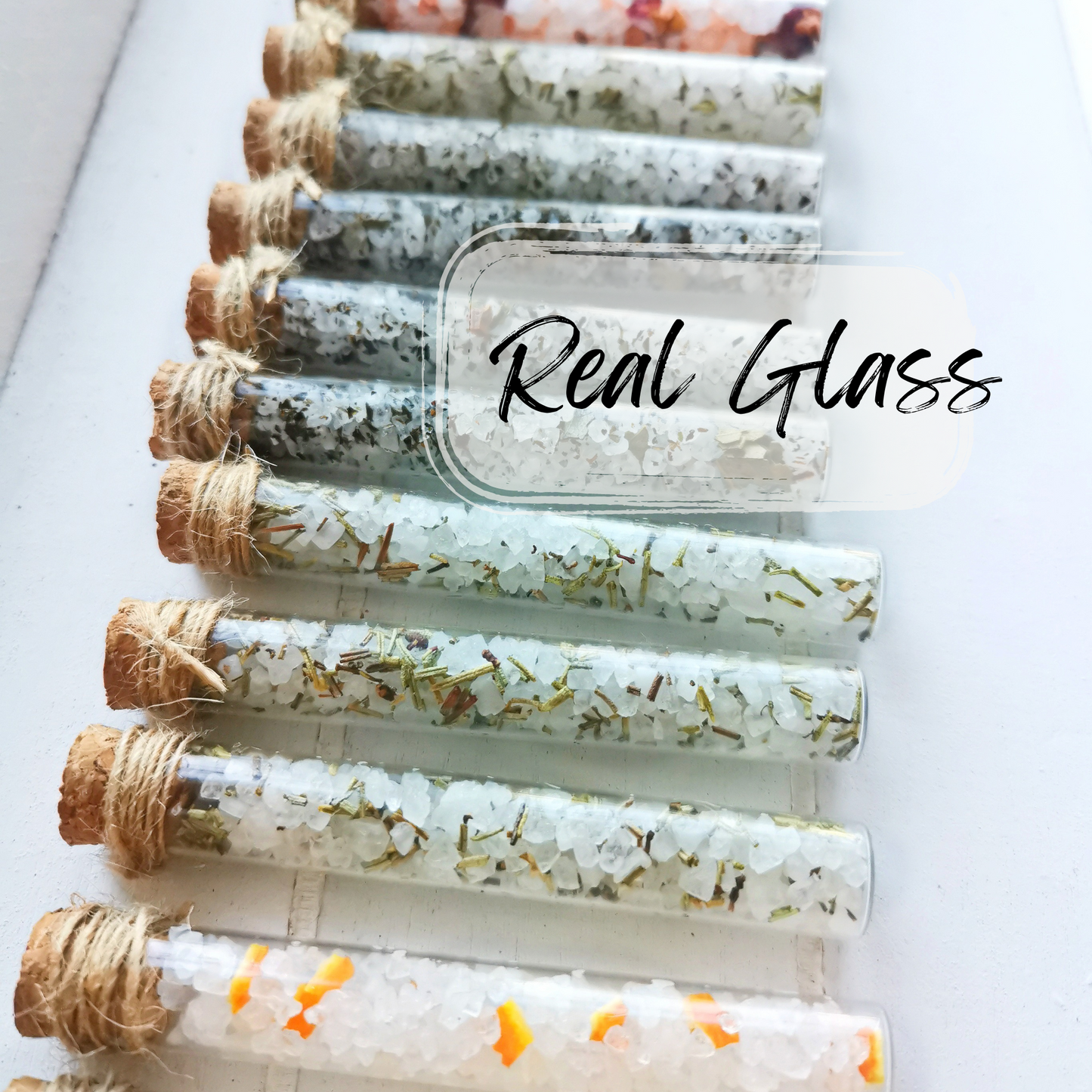 Set of glass vials with cork stoppers containing bath salts on a white background, labeled 'Real Glass'.