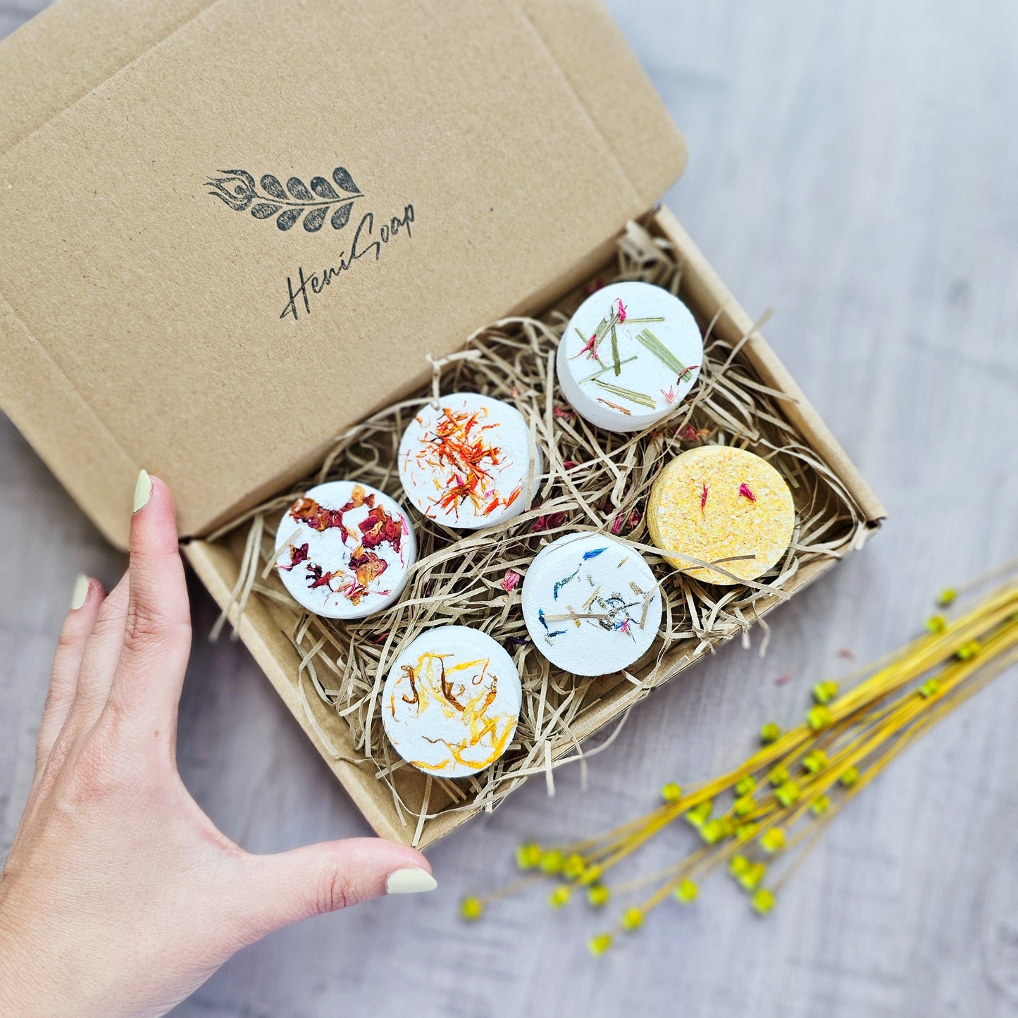 Box of bath bombs with decorative labels on a wooden surface, featuring the brand 'Herbal Soap'.