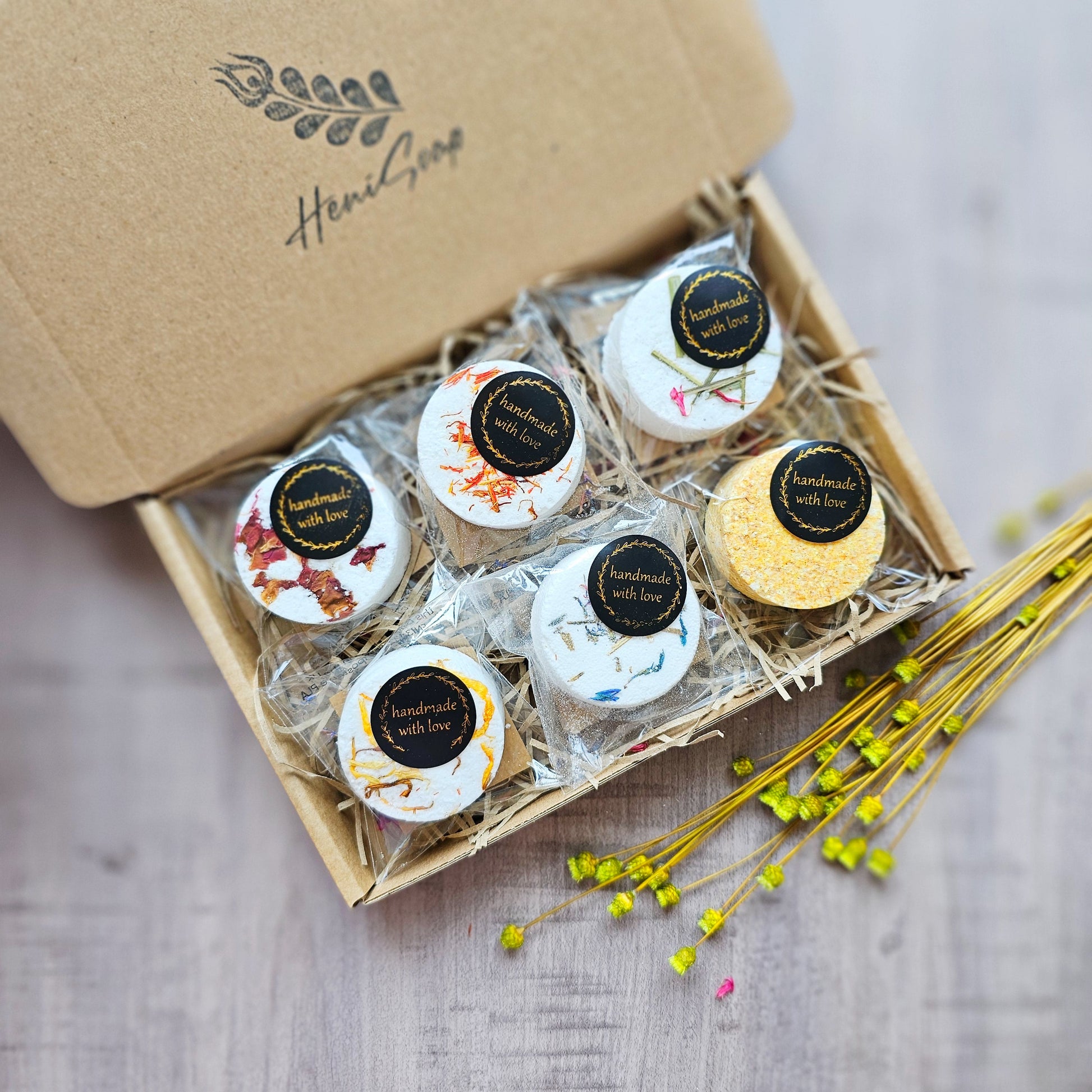 Box of bath bombs with decorative labels on a wooden surface, featuring the brand 'Heni Soap'.
