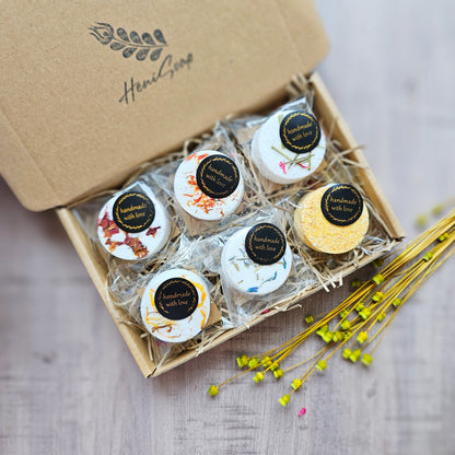 Box of bath bombs with decorative labels on a wooden surface, featuring the brand 'Heni Soap'.