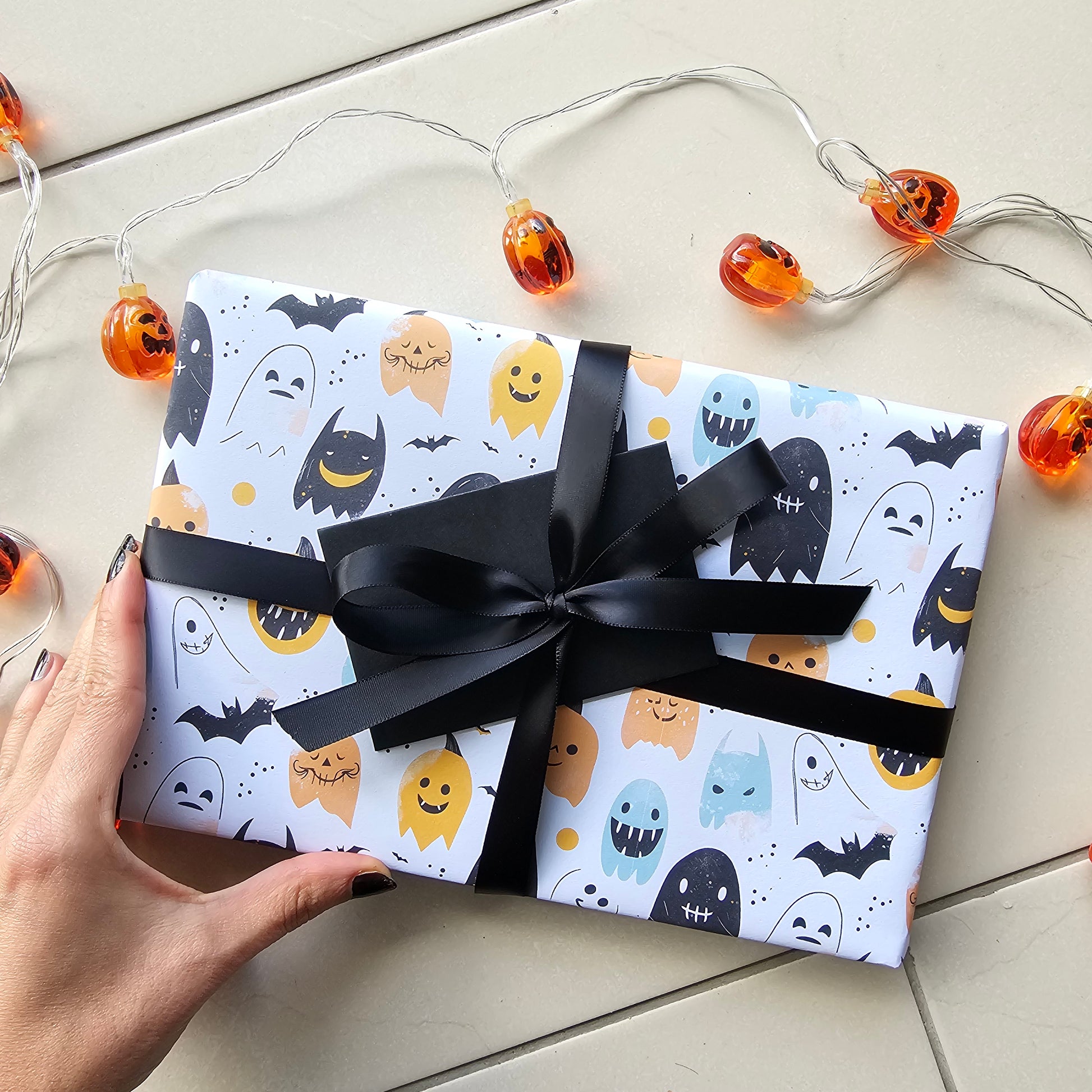 Halloween-themed gift box with a black ribbon held by a hand on a light background.