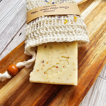Bar of soap with a textured surface on a wooden board, accompanied by a natural fiber soap bag.